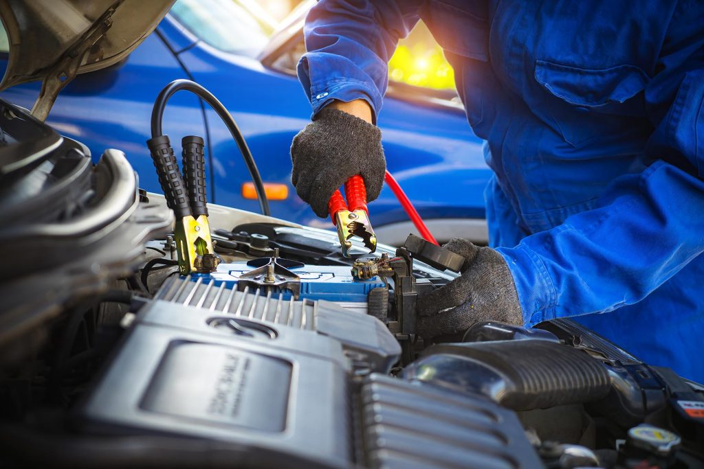 A mechanic connecting jumper cables to a car battery to jump-start the engine