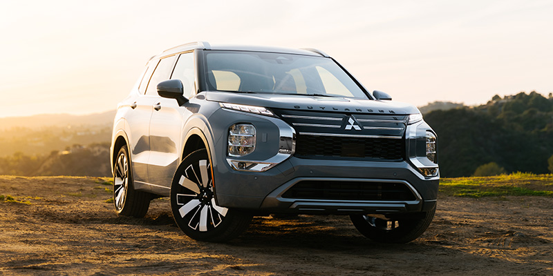 Gray Mitsubishi Outlander SUV parked outdoors at sunset with a scenic landscape background.