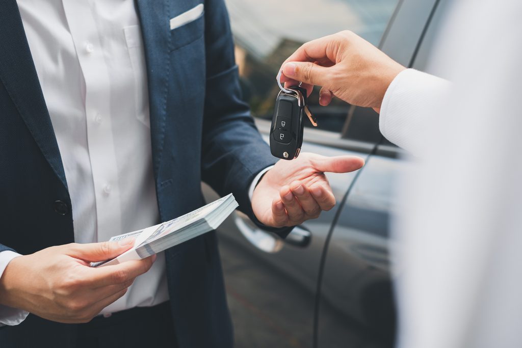 Customer receiving car keys from a salesperson beside a vehicle.
